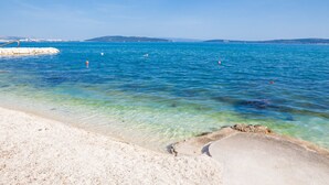 Una spiaggia con acque limpide, una riva sabbiosa e colline in lontananza.