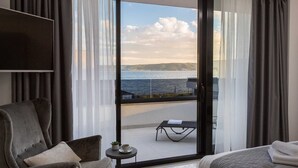Una camera d'albergo moderna con un'ampia porta scorrevole in vetro che si apre su un balcone con vista sul mare.
