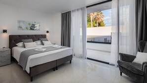 Una camera da letto moderna con un letto grande, un comodino, una sedia e vista sull'esterno tramite una porta scorrevole in vetro.