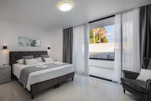 Una camera da letto moderna con un letto grande, un comodino, una sedia e vista sull'esterno tramite una porta scorrevole in vetro.