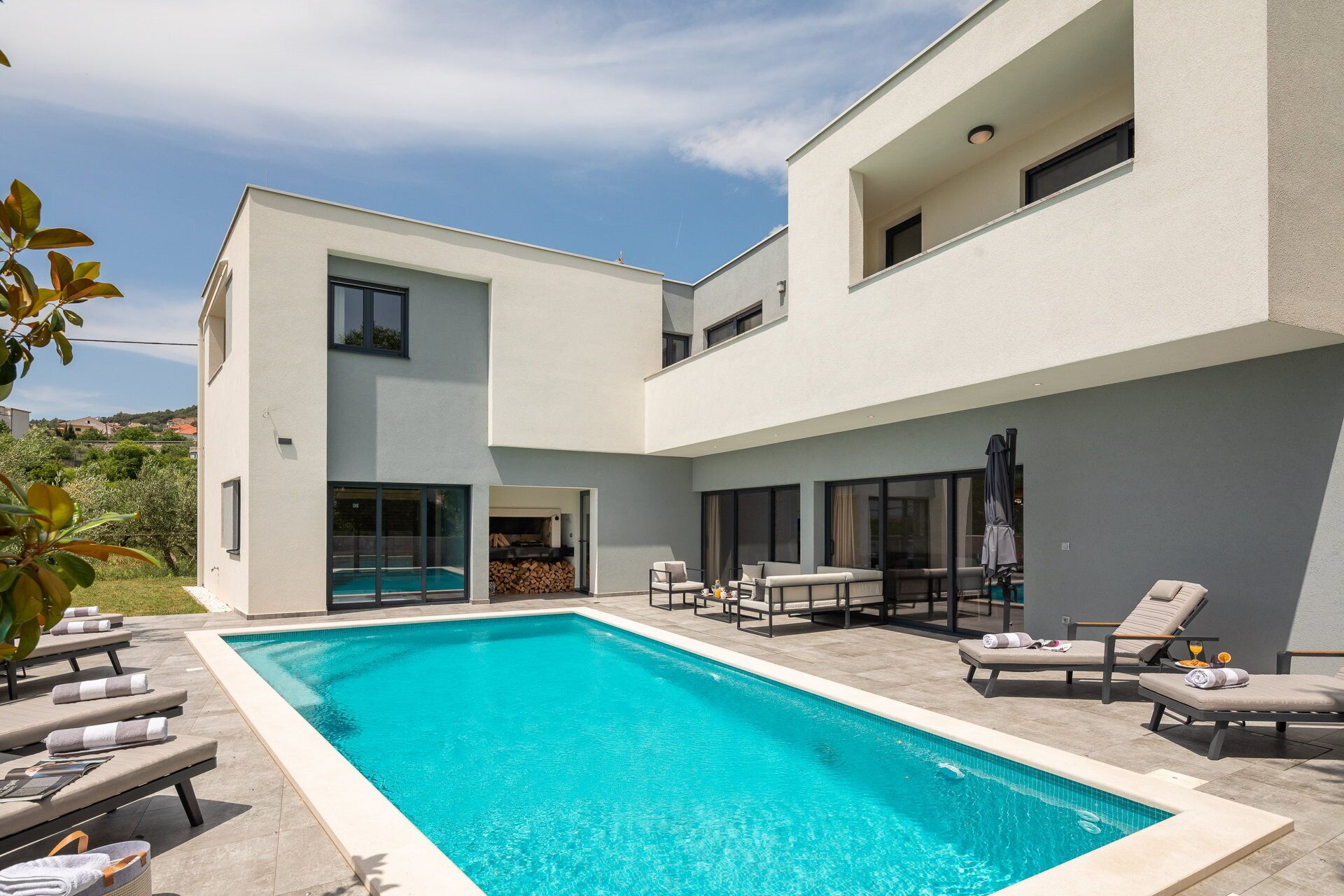 A modern two-story house with a swimming pool, outdoor seating, and a view of the surrounding landscape.