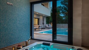 Een modern binnenzwembad met een jacuzzi, ligbedden en uitzicht op een woongebouw.