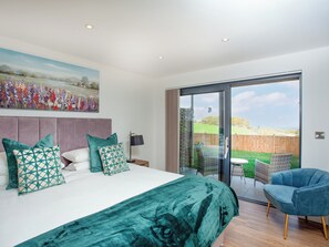 A bedroom with a large bed, a painting, a sliding glass door to a patio, and a blue chair. - 3 bedroom accommodation in Over Stowey, near Bridgwater (Over Stowey, near Bridgwater)