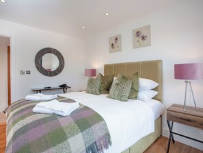 A neatly made bed with a checkered blanket, a bedside table with a lamp, a desk with a phone, and two wall-mounted flower paintings.