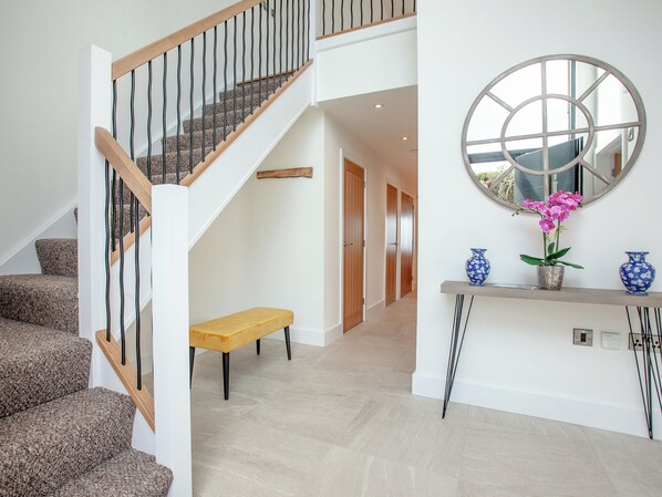 A staircase with wooden railings and carpeted steps, a bench, a console table with vases, and a round mirror on the wall.