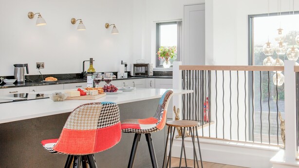 Et moderne køkken med en central ø, barstole og udsigt til det fri.