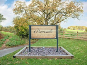 A wooden welcome sign for Bincombe Country Cottages with a paved path and a wooden fence in the background. - 3 bedroom accommodation in Over Stowey, near Bridgwater (Over Stowey, near Bridgwater)