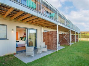 A modern house with a balcony, a glass door entrance, and a patio area with chairs.