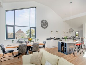 A modern kitchen with a large island, dining area with chairs, and a living room with a sofa.