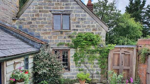 Une maison en pierre avec un petit jardin, une porte en bois et une fenêtre.