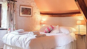 Un lit bien fait, avec du linge de lit blanc et un coussin rose, un tableau encadré au mur et une lampe sur la table de chevet.