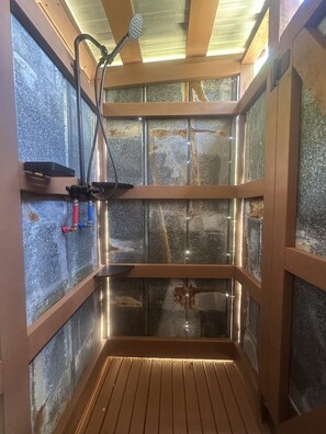 Sauna, jossa on puulattia, kiviseinät ja suihkupää.