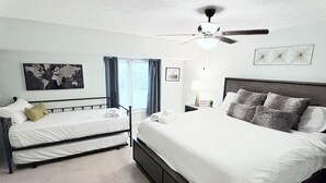 A bedroom with a large bed, a smaller bed, a ceiling fan, a world map on the wall, and a window with curtains. - PRIME Location with Hot Tub, Pool Table and Sauna (Columbus)
