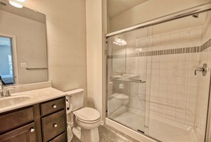 Un baño con ducha de vidrio, inodoro y tocador con cajones.