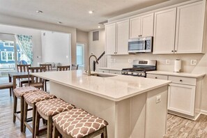A kitchen with a central island, bar stools, a dining area, and a view of the outside.