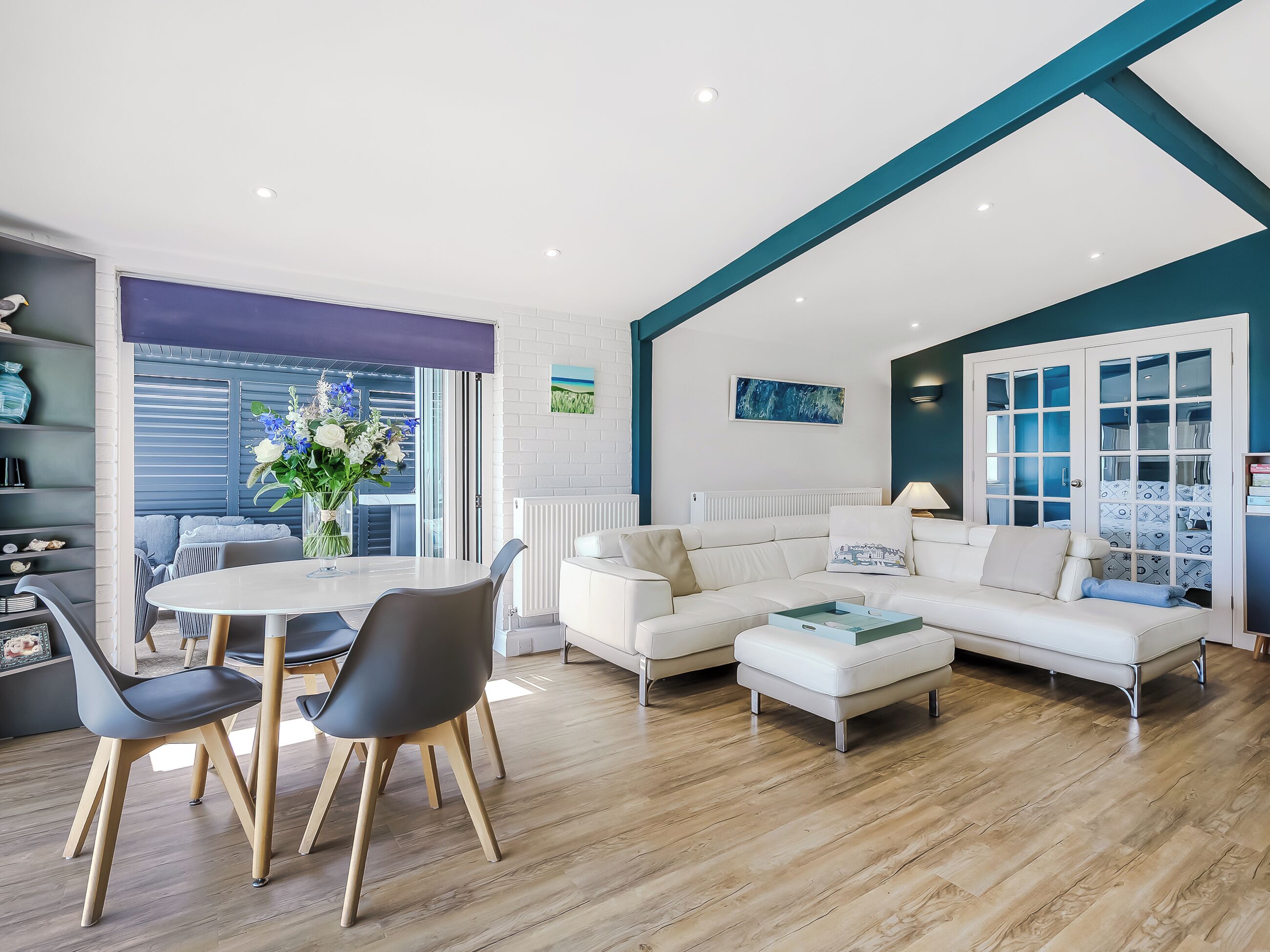 Een moderne woonkamer met een witte bank, een eettafel met stoelen en een groot raam met jaloezieën.