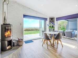 A modern interior with a wood-burning stove, a dining area with chairs, and a view of the outdoors. - Norfolk Broads and Coast, The Beach House (Winterton on Sea)
