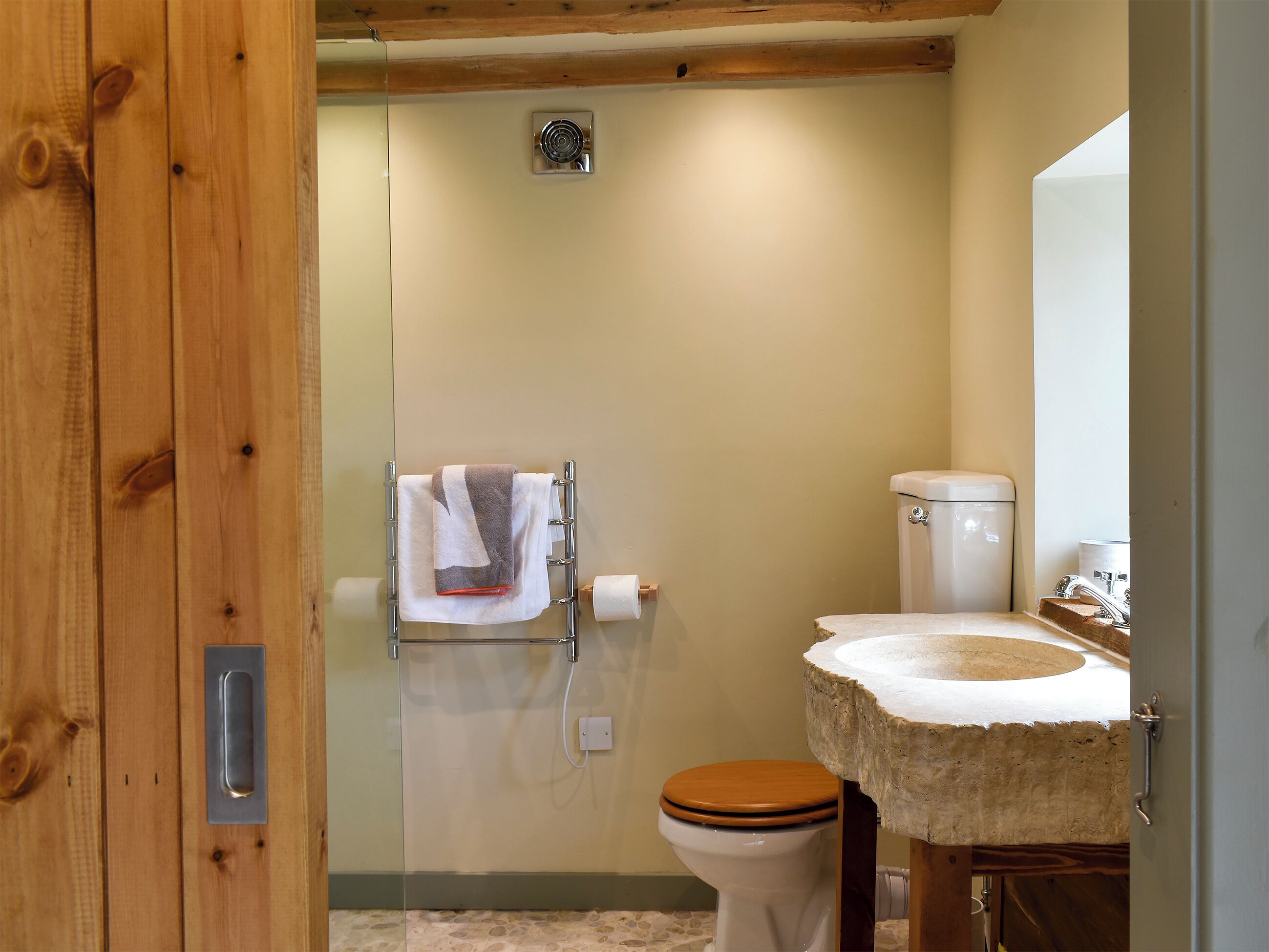 Un bagno con una porta in legno, un water con sedile in legno, un lavabo con piano in pietra e un asciugamano su un portascopevoli.