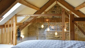 Een kamer met een schuine balken plafond, een stenen muur en een bed met een geborduurde sprei.