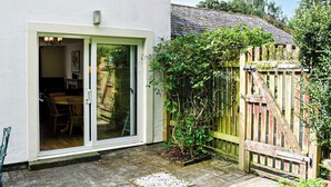 A patio with a wooden table and chairs, a small garden area with a wooden fence, and a sliding glass door leading to an interior space. - 3 bedroom accommodation in Keswick (Keswick)