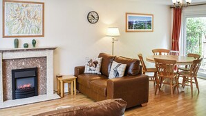 A cozy living room with a fireplace, a sofa, a dining table with chairs, and a clock on the wall. - 3 bedroom accommodation in Keswick (Keswick)