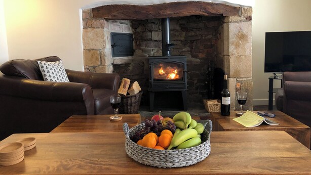 A cozy living room with a stone fireplace, leather sofa, and a fruit bowl on a wooden table. - Church View Cottage & Barn (Hatherleigh, near Okehampton)