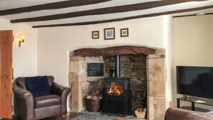A cozy living room with a stone fireplace, leather sofas, and a television. - Church View Cottage & Barn (Hatherleigh, near Okehampton)