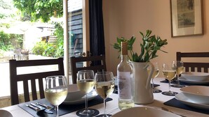 A dining table set with wine glasses, a bottle, and a pitcher, with a view of greenery outside. - Church View Cottage & Barn (Hatherleigh, near Okehampton)