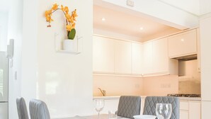 Een moderne eetruimte met een witte tafel, grijs gestoffeerde stoelen en een keuken op de achtergrond.