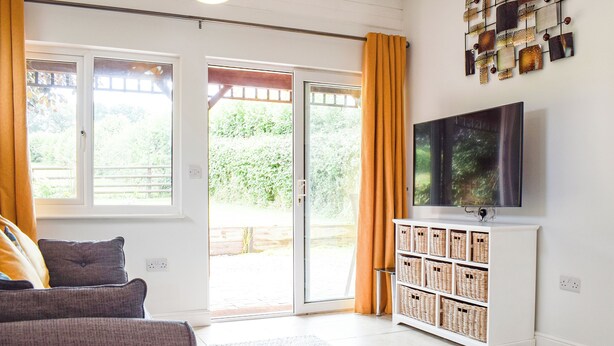 Een kamer met een bank, een televisie, een wandplank met manden en een glazen schuifdeur naar een buitenruimte.