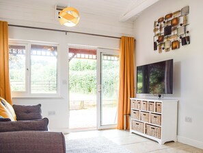 Een kamer met een bank, een televisie, een wandplank met manden en een glazen schuifdeur naar een buitenruimte.
