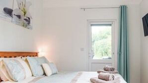 Een slaapkamer met een bed, kussens, een raam en een deur.