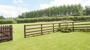 Een omheind gazon met een houten poort, een bankje en een haag op de achtergrond.