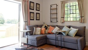 A living room with a grey sectional sofa, a black leather rug, a wooden side table, a hanging red light fixture, and a window with curtains.