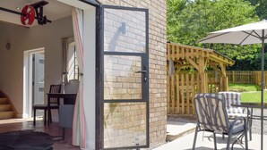 An open sliding glass door leading to a patio area with outdoor furniture and a wooden fence.