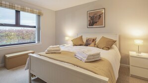 Un dormitorio con cama, lámparas de noche, ventana con vistas, un banco y un cuadro en la pared.