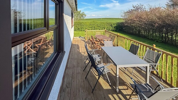 Una terraza de madera con una mesa y sillas, con vistas a un paisaje verde.