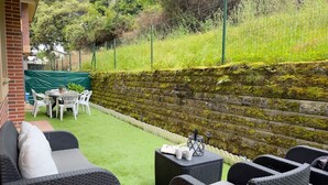 Un patio con mobiliario exterior, un muro de piedra y una valla verde.