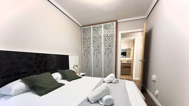 Una habitación de hotel moderna con una cama grande, dos almohadas, un cabecero gris y un separador decorativo.