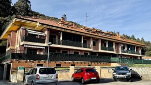 Un edificio de varios pisos con techo de tejas, un estacionamiento con varios autos y un cartel que indica 'Villa Mercedes'.