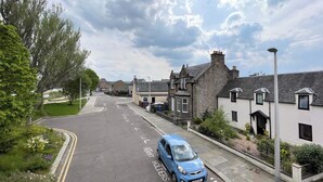 Une rue résidentielle bordée de maisons, une voiture bleue garée sur le côté et un ciel dégagé.