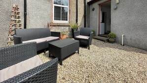 Un espace extérieur aménagé en terrasse, avec des meubles en osier, une échelle et une plante en pot.