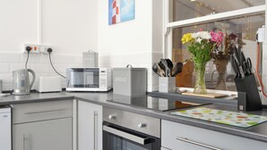 A modern kitchen with a microwave, toaster, kettle, and oven. There is a vase with flowers on the counter and a window with a view of a lighthouse. - 2 bedroom accommodation in Filey (Filey)