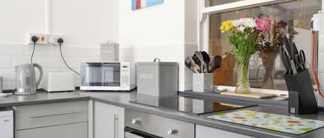 A modern kitchen with a kettle, toaster, microwave, and oven. There is a window with a view of a lighthouse and a vase with flowers on the counter.