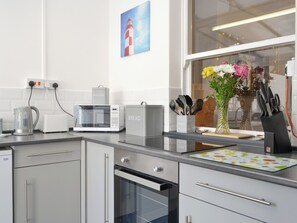Una cocina moderna con microondas, tostadora, tetera y horno. Hay un florero con flores en la encimera y una ventana con vistas a un faro.
