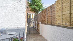 A narrow outdoor patio with a round table and chairs, a white brick wall, and a wooden fence. - 2 bedroom accommodation in Filey (Filey)