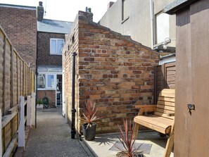 A narrow alleyway with a brick wall, a wooden bench, and a potted plant.