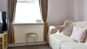 A room with a beige sofa, a small round table, a TV on a stand, and a window with curtains. - 2 bedroom accommodation in Filey (Filey)