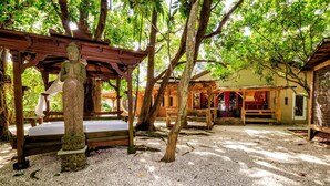 A traditional Japanese garden with a stone statue, wooden benches, and a covered seating area. -  Tiny House in Authentic Japanese Koi Garden in Florida (Homestead)