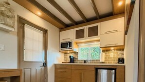 A kitchen with wooden cabinets, a stainless steel refrigerator, a microwave, and a window with a view of greenery. -  Tiny House in Authentic Japanese Koi Garden in Florida (Homestead)